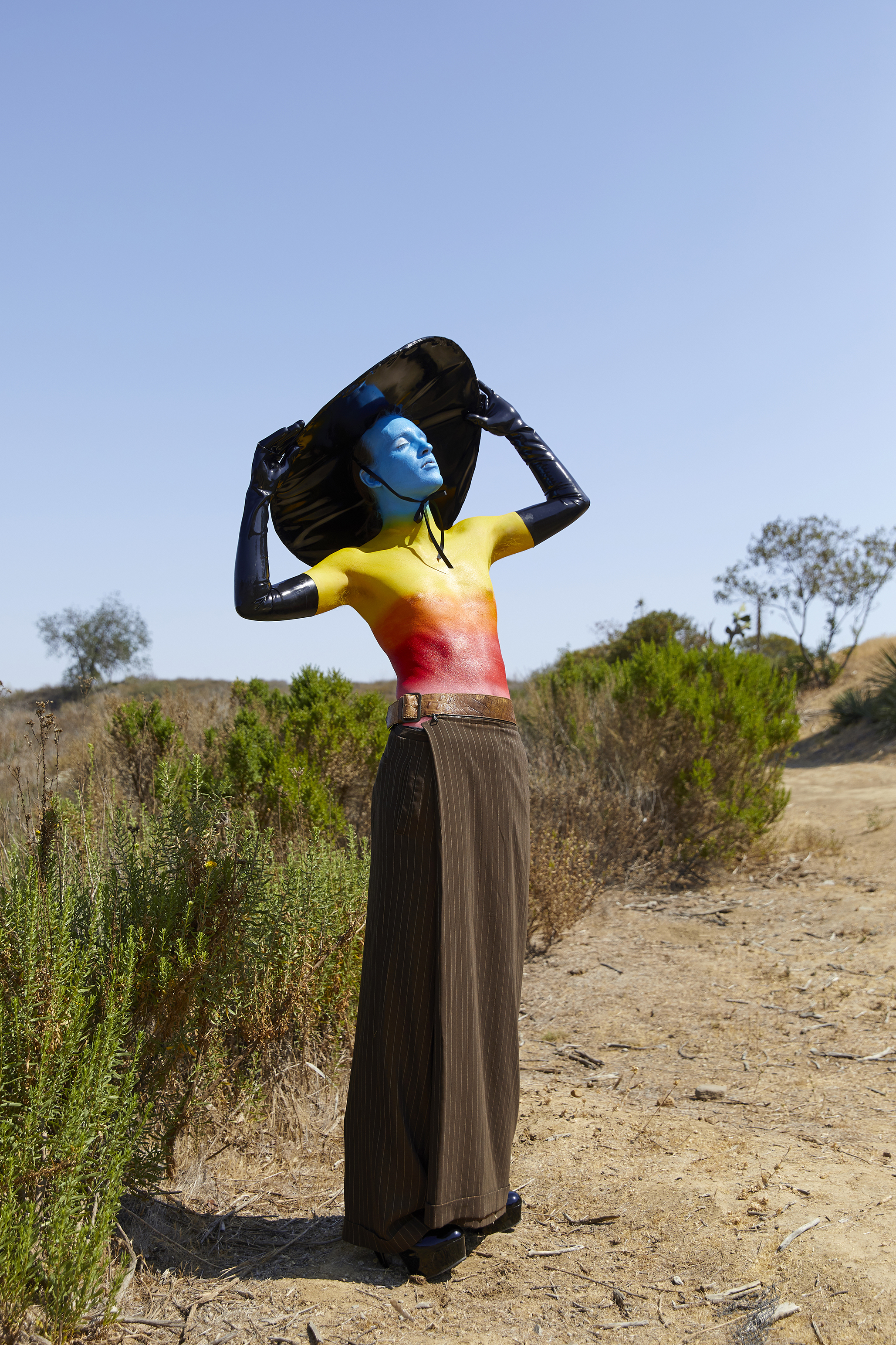 Jesse shirtless with rainbow body paint, latex hat and gloves outside posing